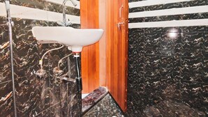 A bathroom with a white sink, black marble walls, and a wooden door. - Hotel Royal Krishna (Gorakhpur)