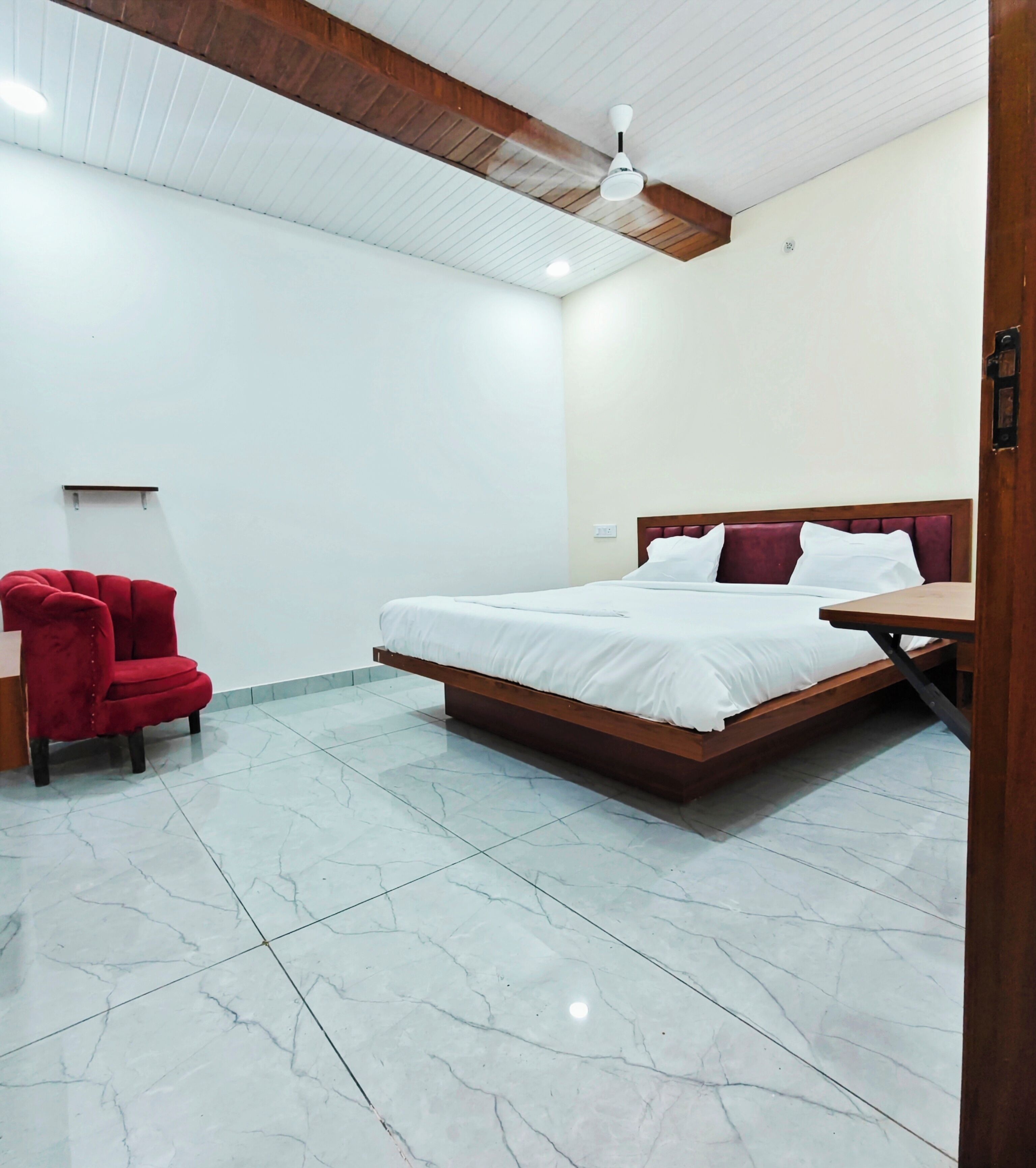 Une chambre à coucher avec un lit, une chaise rouge, une table de chevet en bois et un ventilateur de plafond.
