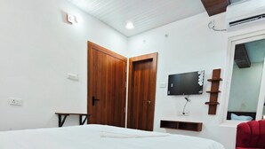 A bedroom with a large bed, wooden doors, a TV mounted on the wall, and a red chair. - Hotel Royal Krishna (Gorakhpur)