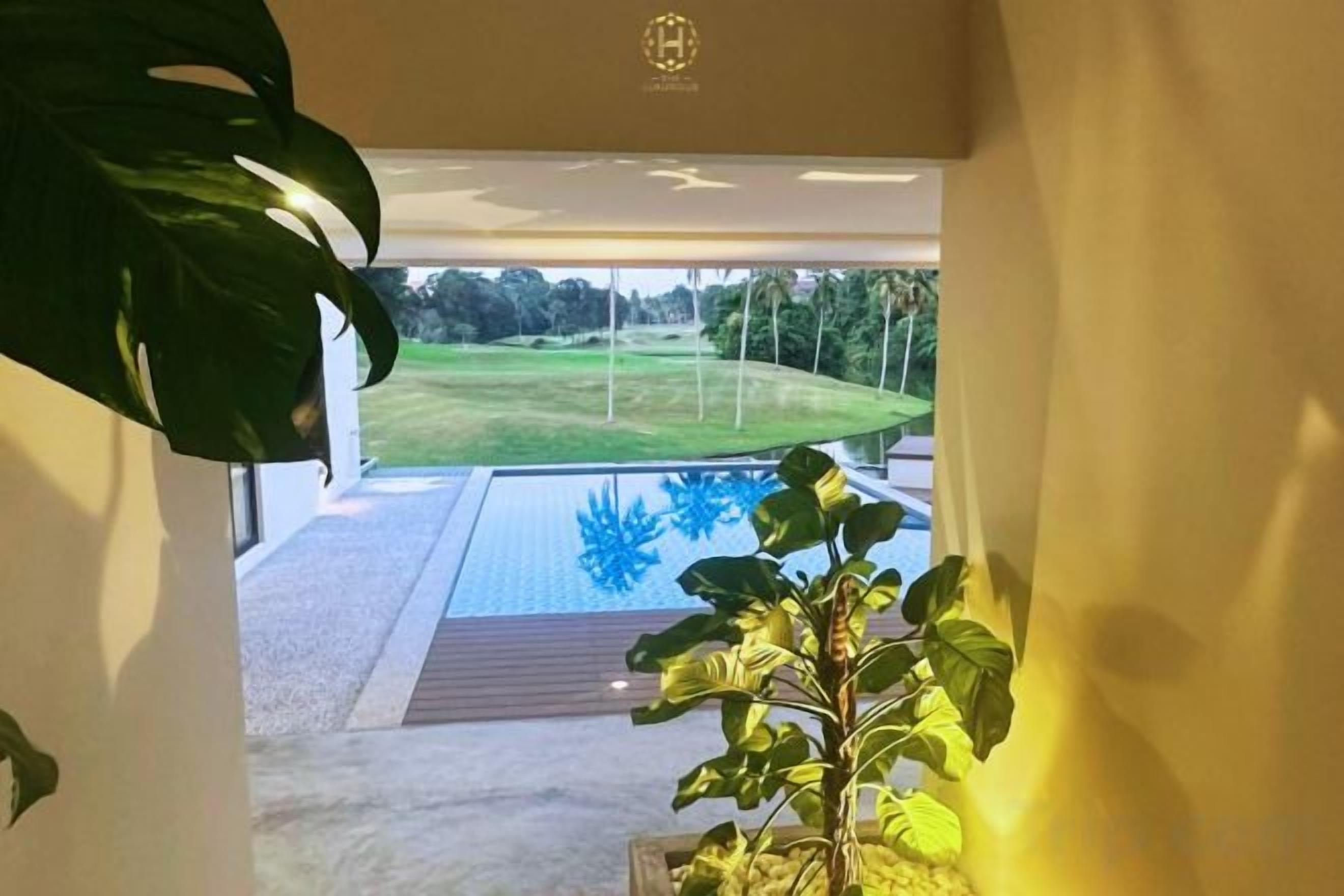 Vista da una stanza su un'area piscina con un solarium in legno e un prato.