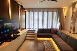 Una sala de estar moderna con un televisor de pantalla plana, un sofá, una escalera y un gran ventanal con cortinas.