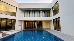 A modern building with a central swimming pool, large windows, and a staircase leading to an upper level. - The Luxurious 231, Lake House Villa (Pegoh)