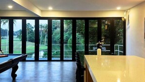 A modern room with a pool table, a bar area, and large windows offering a view of a lush garden. - The Luxurious 231, Lake House Villa (Pegoh)