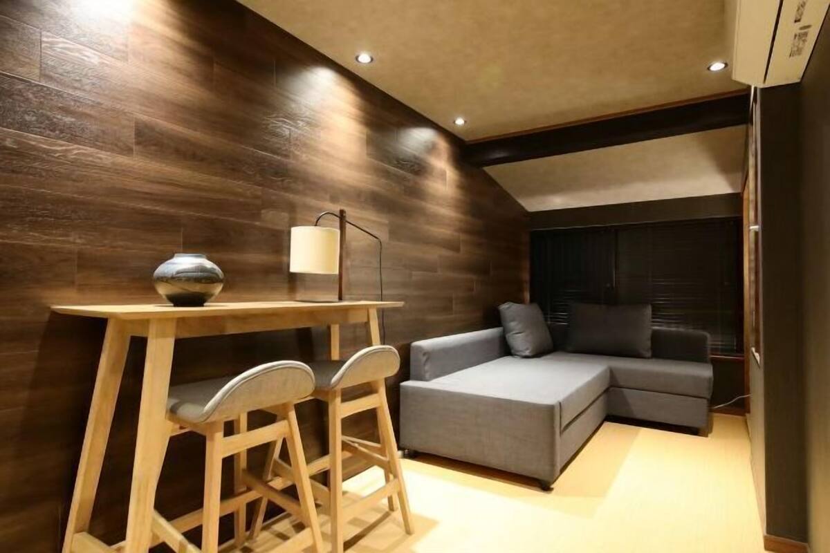 A modern interior with a wooden wall, a gray sofa, a small wooden table with two chairs, and a floor lamp.