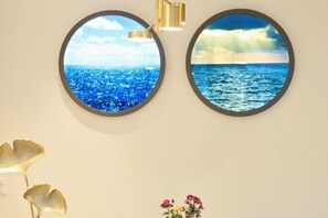 Deux œuvres d’art murales de forme circulaire représentant des scènes marines, un lustre doré et un vase rempli de fleurs.
