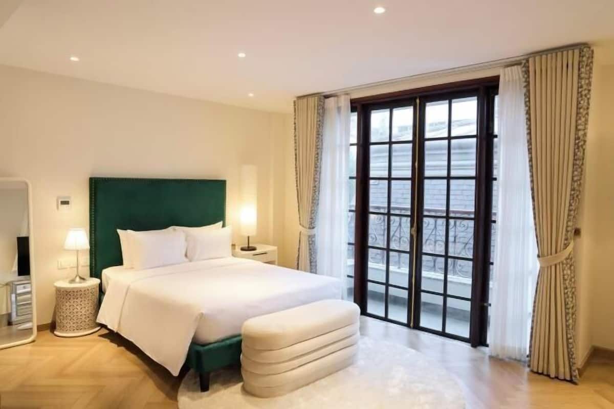 Ein Hotelzimmer mit einem großen Bett, einem grünen Kopfteil, einem Fenster mit Vorhängen und Blick nach draußen.