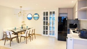 Een moderne keuken met een zwarte koelkast, witte kasten en een eethoek met een glazen tafel en stoelen.