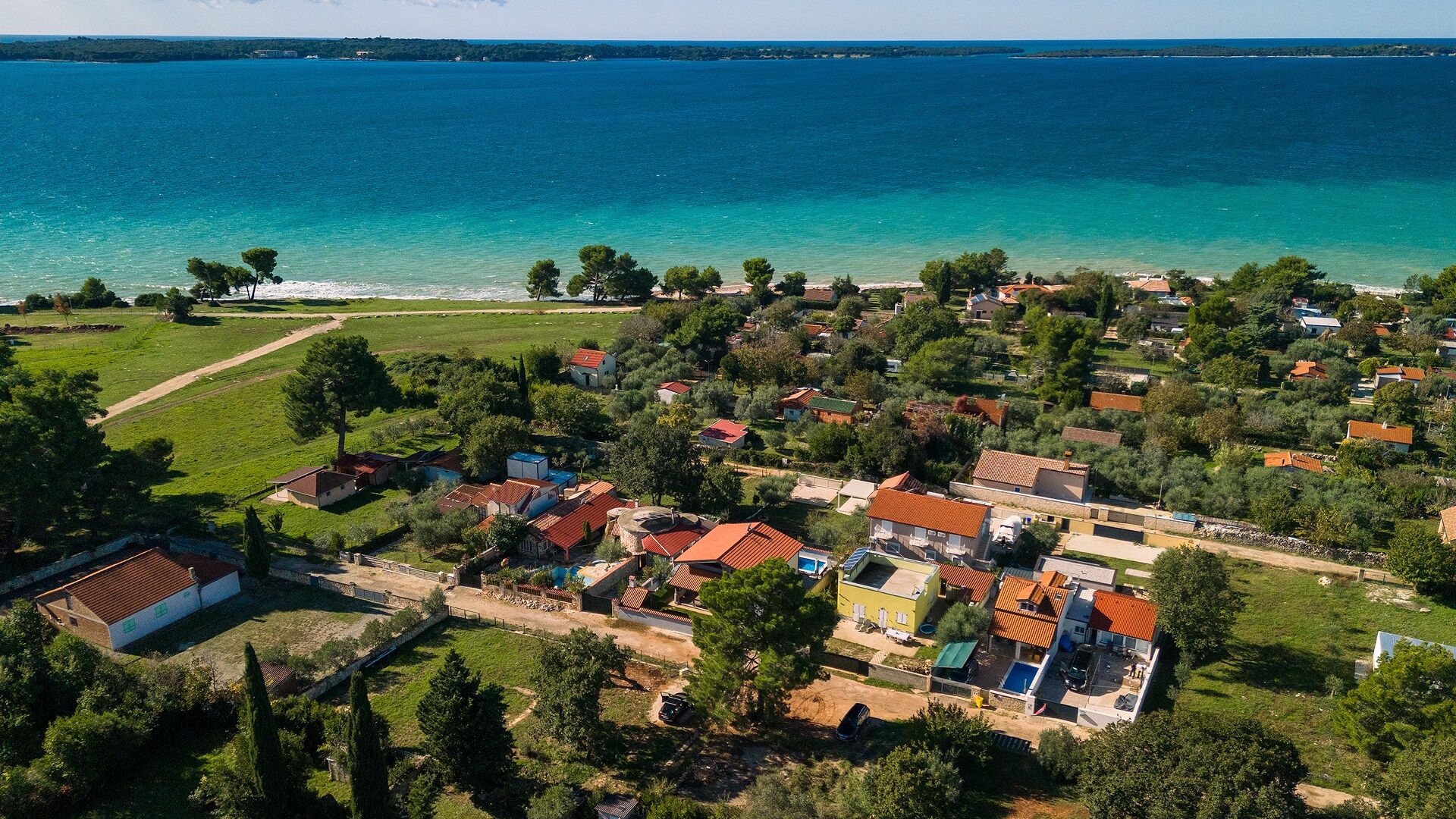An aerial view of a coastal village with houses, a beach, and a clear view of the sea.