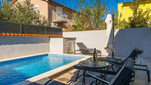 A swimming pool with lounge chairs and a table, surrounded by a low wall and a building with balconies. - Villa Katarina - Peroj by Villas Guide (Peroj)
