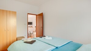 A bedroom with two beds, a wooden wardrobe, a bathroom visible through an open door, and a television in the bathroom. - Villa Katarina - Peroj by Villas Guide (Peroj)