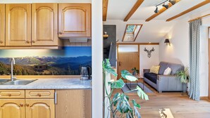 A kitchen with wooden cabinets and a view of mountains, a living room with a sofa and plants, and a ceiling with exposed beams and lighting.