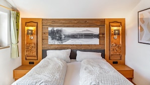 A double bed with a wooden headboard, two bedside tables, a framed landscape painting, and wall-mounted reading lights.