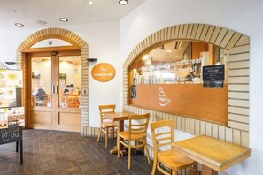 Interior de una cafetería con muebles de madera, una barra con un menú y una puerta visible que da al exterior.
