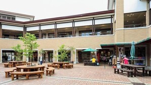 Ein Innenhof mit Holzbänken und -tischen, umgeben von einem Gebäude mit großen Fenstern und einer Ziegelwand.