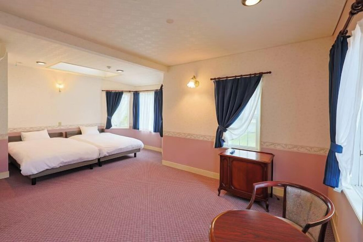 Een hotelkamer met twee bedden, een klein houten tafeltje en een stoel.