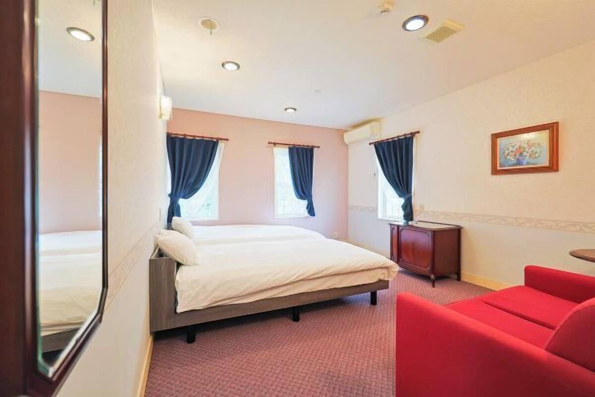 Une chambre d’hôtel avec un lit, une chaise rouge, une petite table et un tableau au mur.