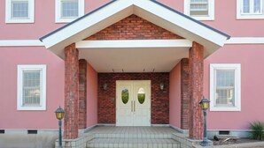 Un bâtiment à la façade rose, avec une entrée en briques et une porte blanche dotée de deux fenêtres.