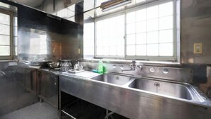 Une cuisine professionnelle en acier inoxydable, équipée de deux éviers, d’une fenêtre et d’un système de ventilation au plafond.
