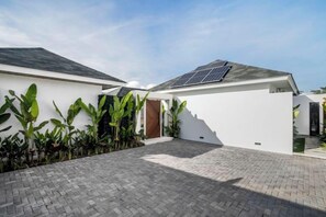 A modern house with a paved driveway, a solar panel on the roof, and a small garden area with tropical plants. - Villa Nature View by BaliSuperHost (Bali)