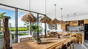 A modern kitchen with a large island, wooden dining table, and hanging thatched lights. - Villa Nature View by BaliSuperHost (Bali)