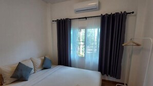 A hotel room with a bed, a window with curtains, a wall-mounted air conditioner, and a clothing rack. - Raiyaa Farmstay (Kaeng Krachan)
