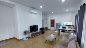 A modern living room with a flat-screen TV, a fan, a sofa, and a dining area with a table and chairs. - Raiyaa Farmstay (Kaeng Krachan)