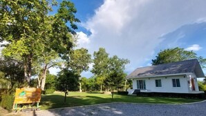 A white house with a grey roof, surrounded by a well-maintained lawn and trees. - Raiyaa Farmstay (Kaeng Krachan)