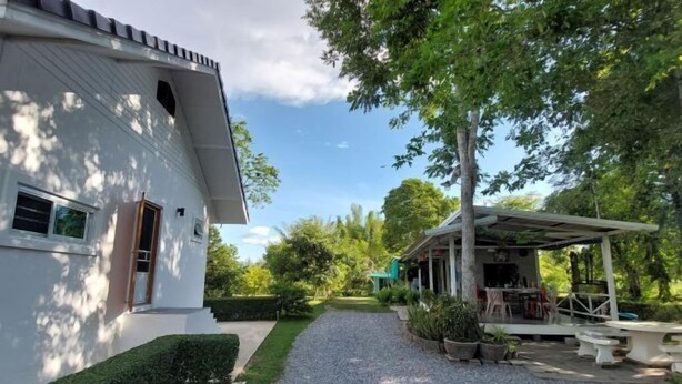 A white building with a covered outdoor seating area and a gravel path leading to it. - Raiyaa Farmstay (Kaeng Krachan)