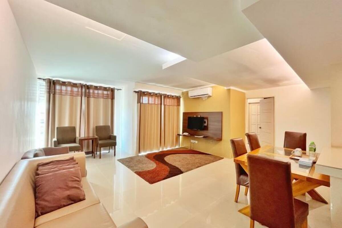 A modern living room with a sofa, chairs, a dining table, and a flat-screen TV.