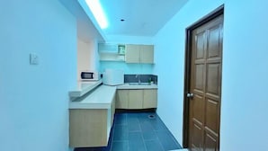 A narrow kitchen with a microwave, cabinets, and a sink. - Official Khalifa Suites Hotel & Apartment (Kota Bharu)