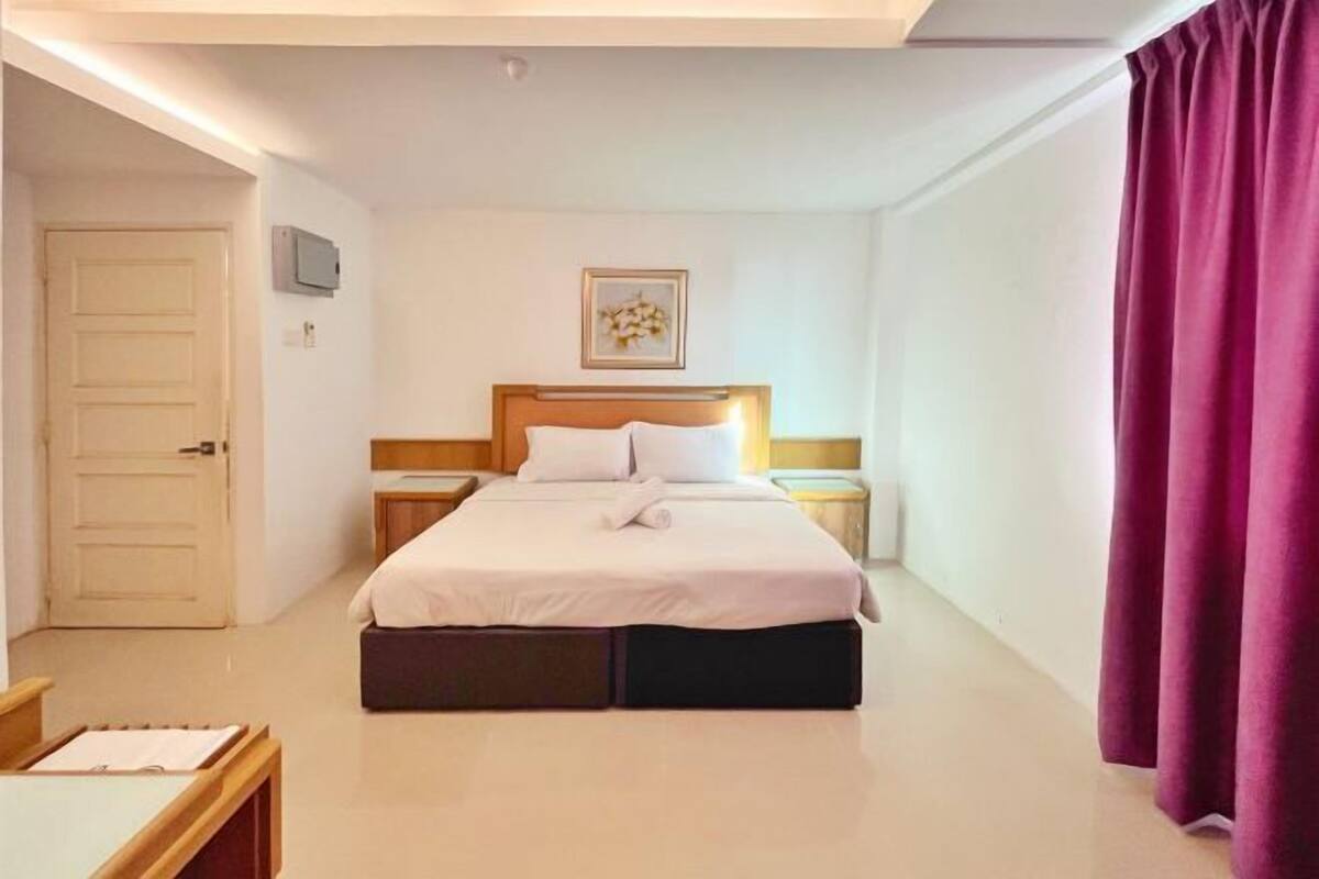 A hotel room with a bed, bedside tables, a door, a light switch, and a wall-mounted light fixture.