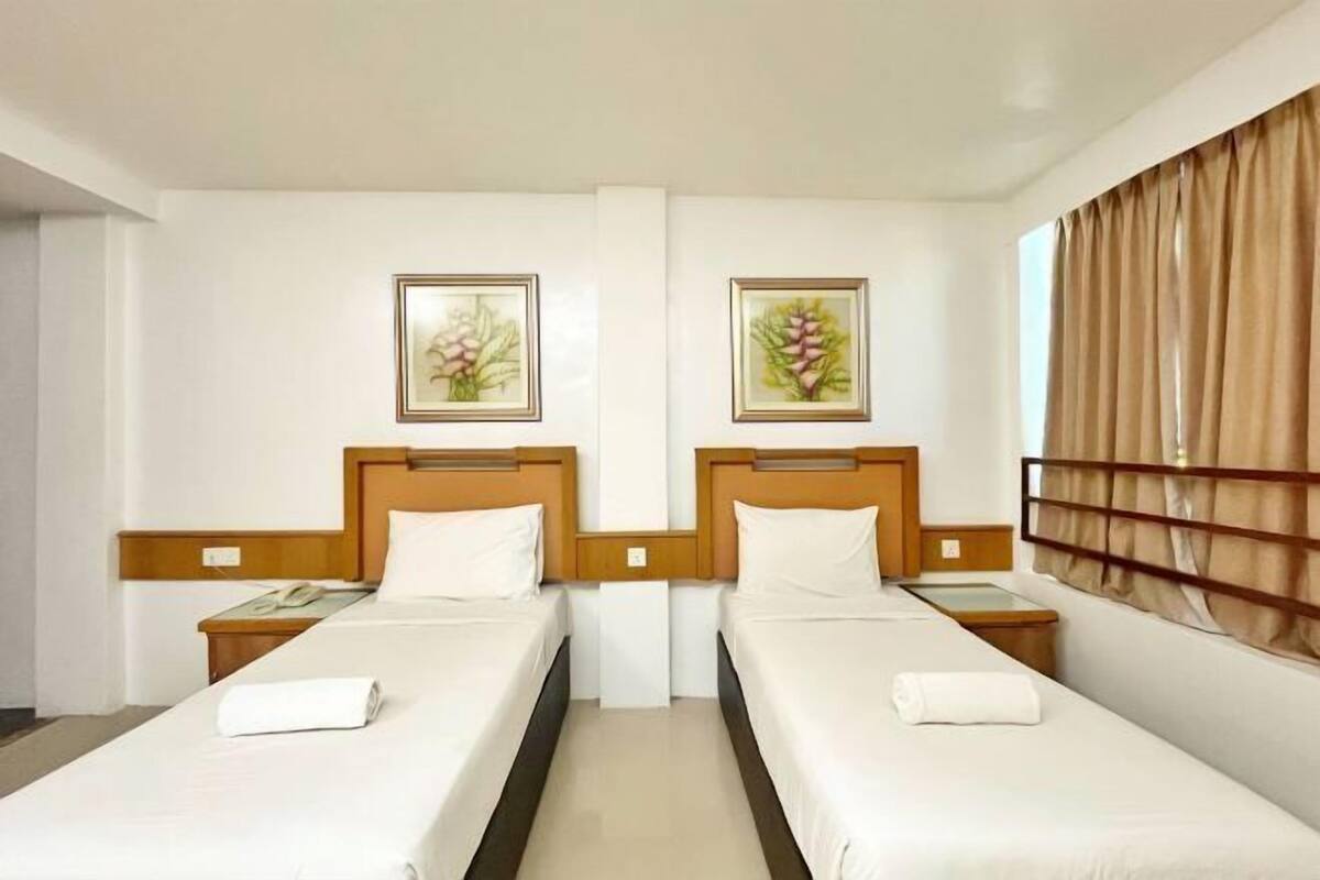 A hotel room with two beds, a wooden headboard, a nightstand with a phone, and a window with curtains.