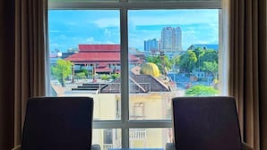 A room with a large window, two chairs, and a view of a cityscape with buildings and a red-roofed structure. - Official Khalifa Suites Hotel & Apartment (Kota Bharu)