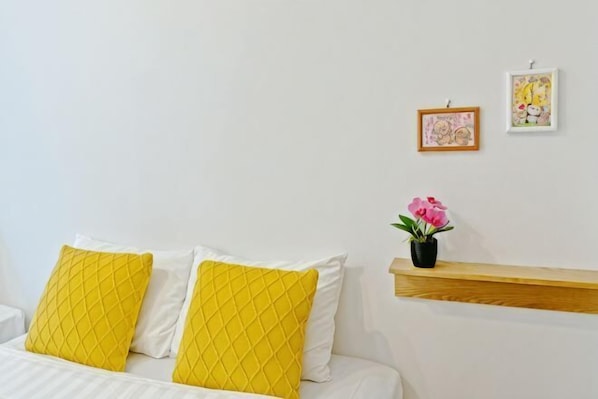 A bed with yellow and white pillows, a small potted plant, and two framed pictures on the wall.
