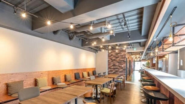 Un restaurante moderno con largas mesas de madera y taburetes de bar, una pared de acento de ladrillo e iluminación colgante.