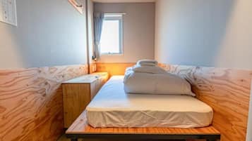A small, compact room with a single bed, a wooden bench, and a window providing natural light.