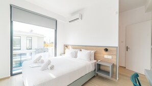 A modern hotel room with a large bed, a bedside table, a nightstand, and a view of the outside.