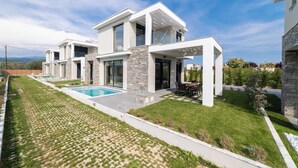 A modern two-story house with a swimming pool, stone pillars, and a well-maintained lawn.