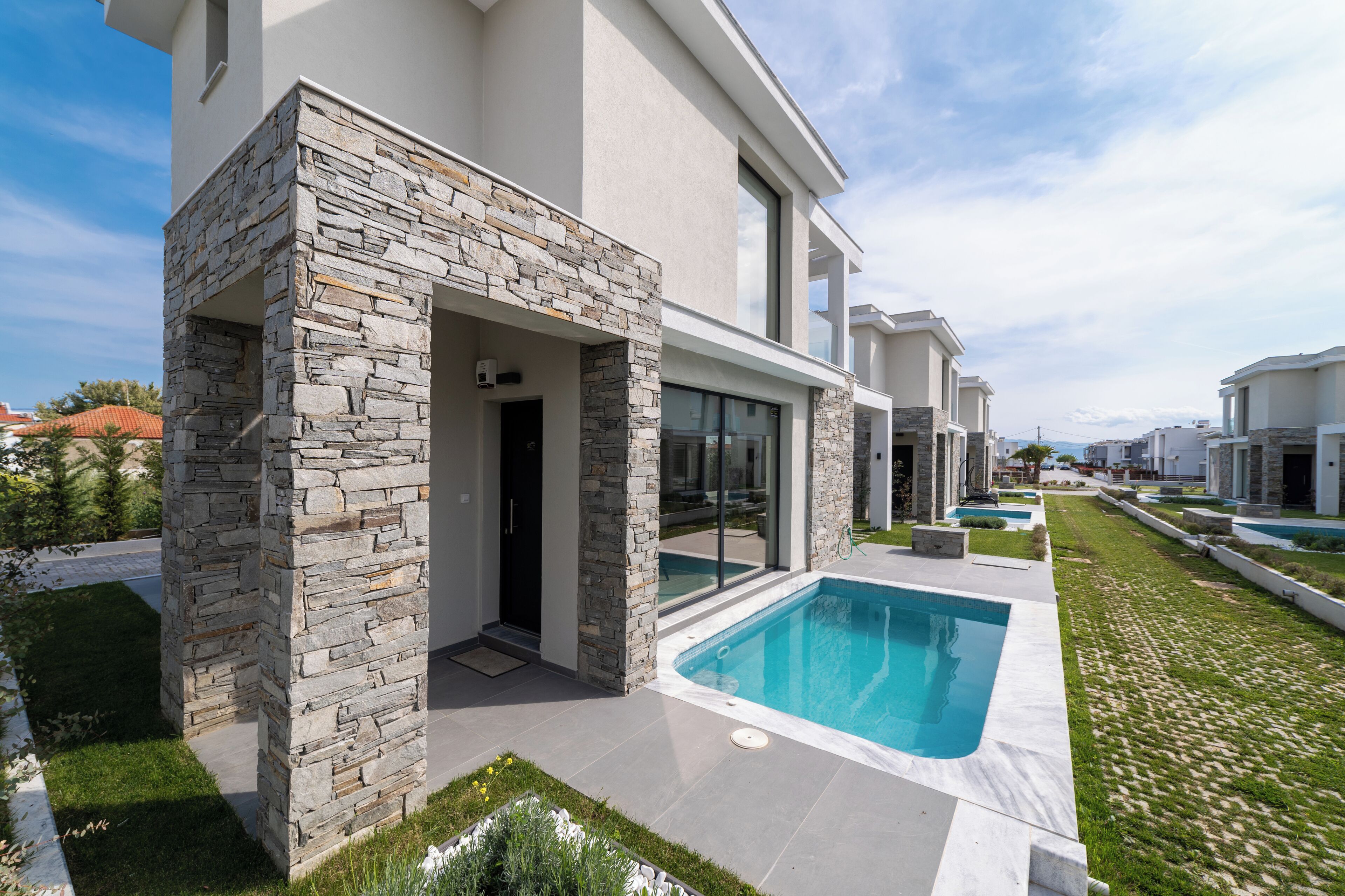 Una casa moderna con fachada de piedra, piscina y césped cuidado.