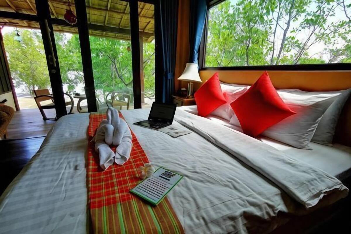 Une chambre d’hôtel avec un lit, un ordinateur portable, un oreiller rouge et une vue sur les arbres.