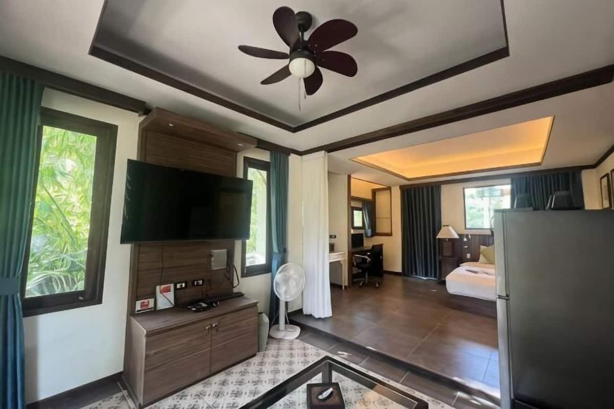 Une chambre d’hôtel équipée d’une télévision à écran plat, d’un ventilateur de plafond, de grandes fenêtres et d’un coin repas.