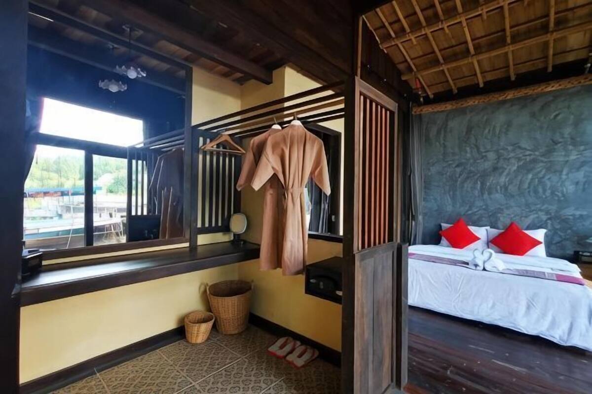 Une pièce avec un lit, une fenêtre, une robe suspendue, un panier et un plancher en bois.