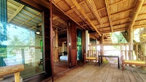A wooden deck with a thatched roof, wooden benches, and a view of the outdoors.