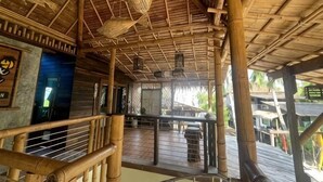 A bamboo structure with a thatched roof, a balcony, and a view of the surrounding area.