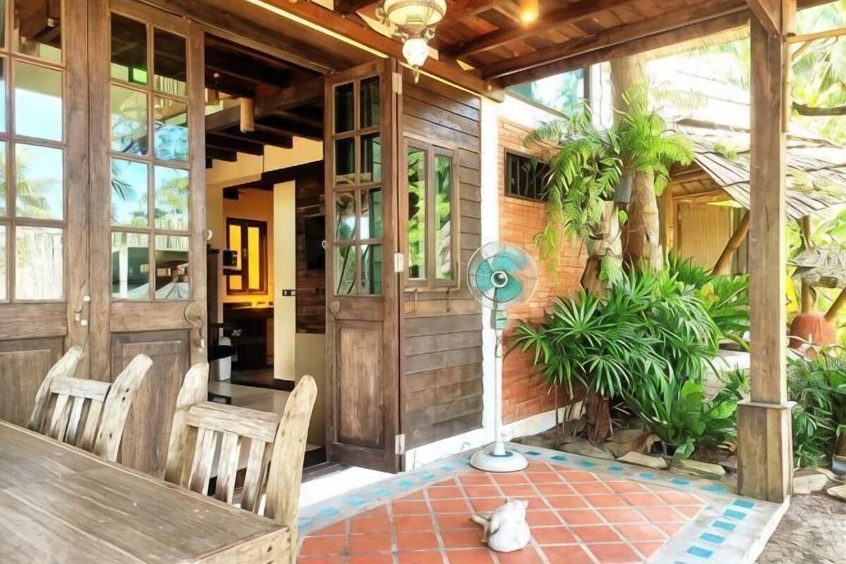 Une structure extérieure en bois comprenant une table et des chaises, un ventilateur et des plantes en pot.