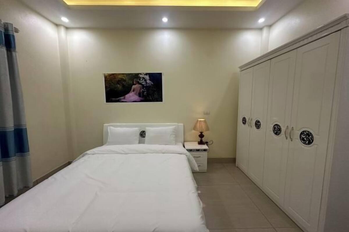 A bedroom with a bed, a nightstand with a lamp, a wardrobe, and a painting on the wall.