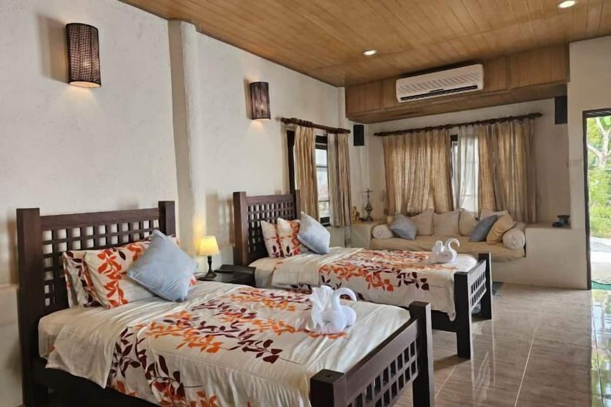 A hotel room with two beds, a sofa, a table, and a view of the outdoors.