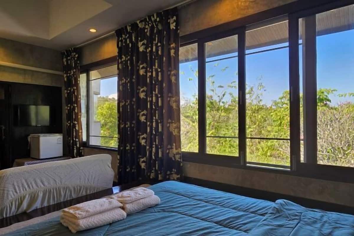 A bedroom with a bed, a TV, and a window with a view of greenery.