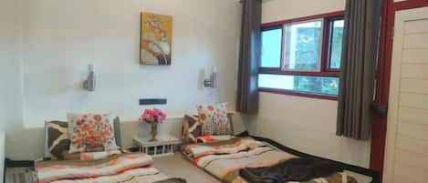 A room with two beds, a small table with a vase, and a window with curtains.