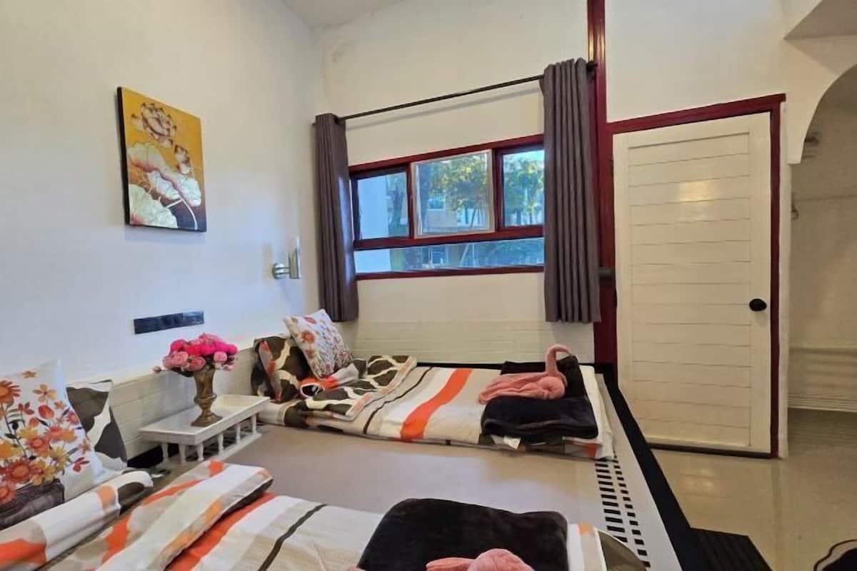 A room with a bed, a sofa, a small table with a vase, a window with curtains, and a door.
